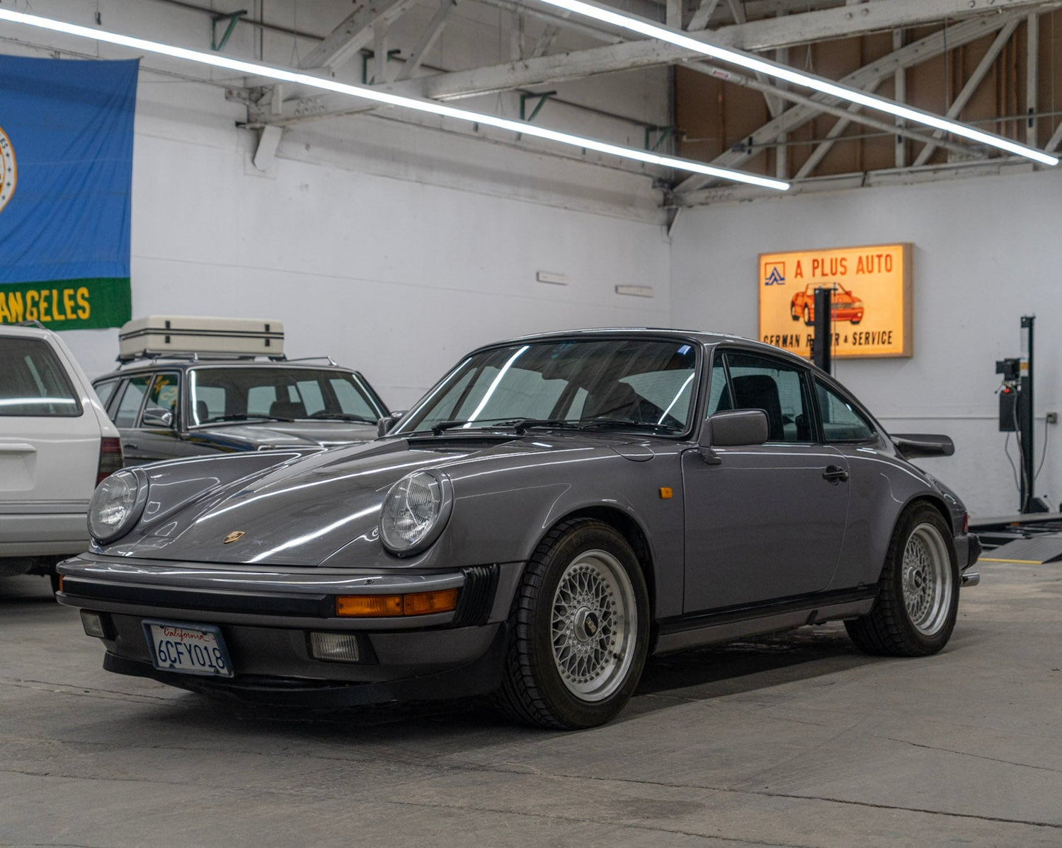 Gray Porsche car in a garage with various signs and flags on the wall.